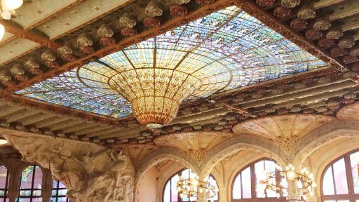 The Glow Worm looks like a droplet of water that is forever waiting to fall. This gorgeous glass construction dominates the ceiling. The droplet of the Glow Worm is like The Palau’s own sun, surrounded by a choir of stained glass women that sing its praises.